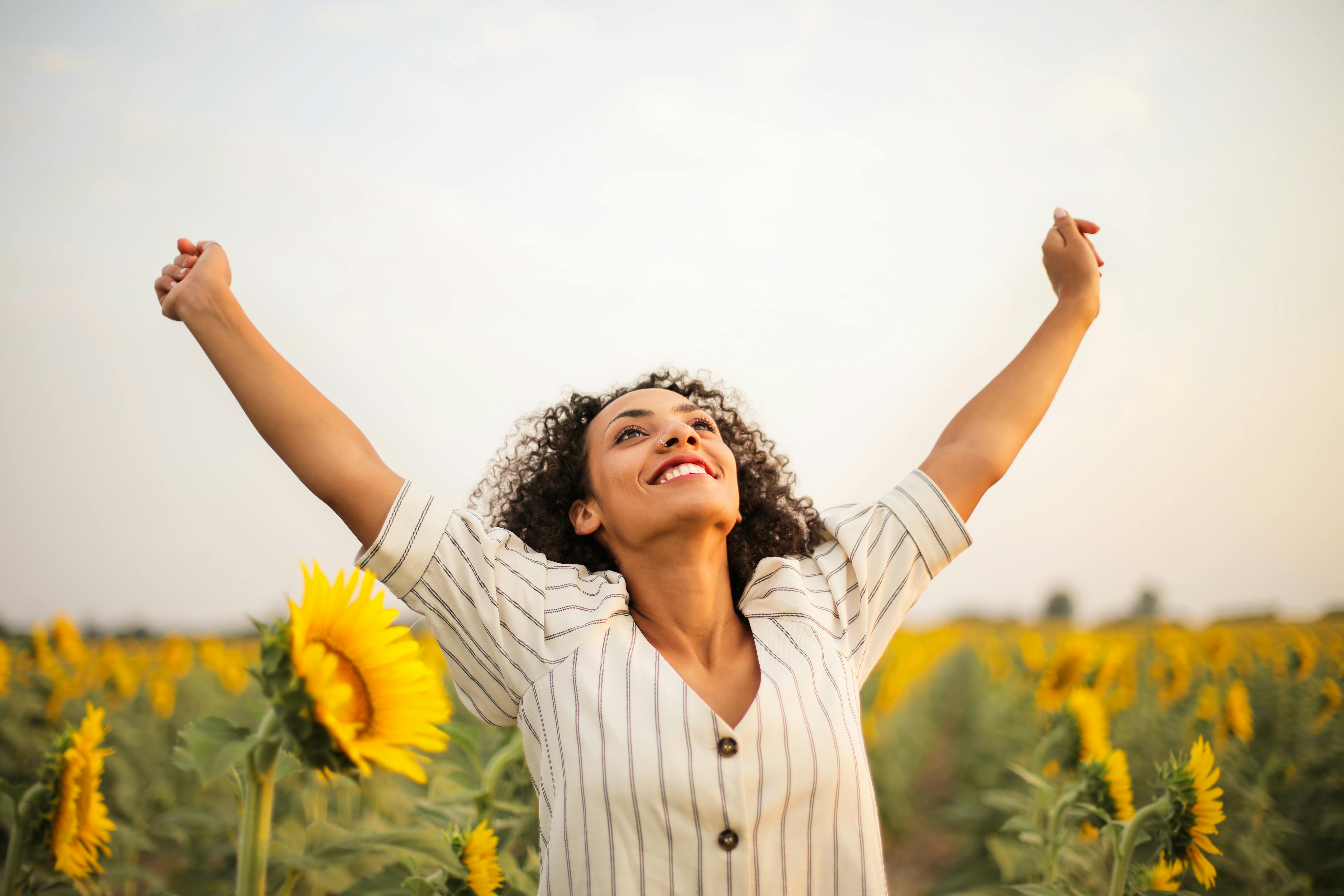 Woman with arms raised in sunflower field — healing and joy