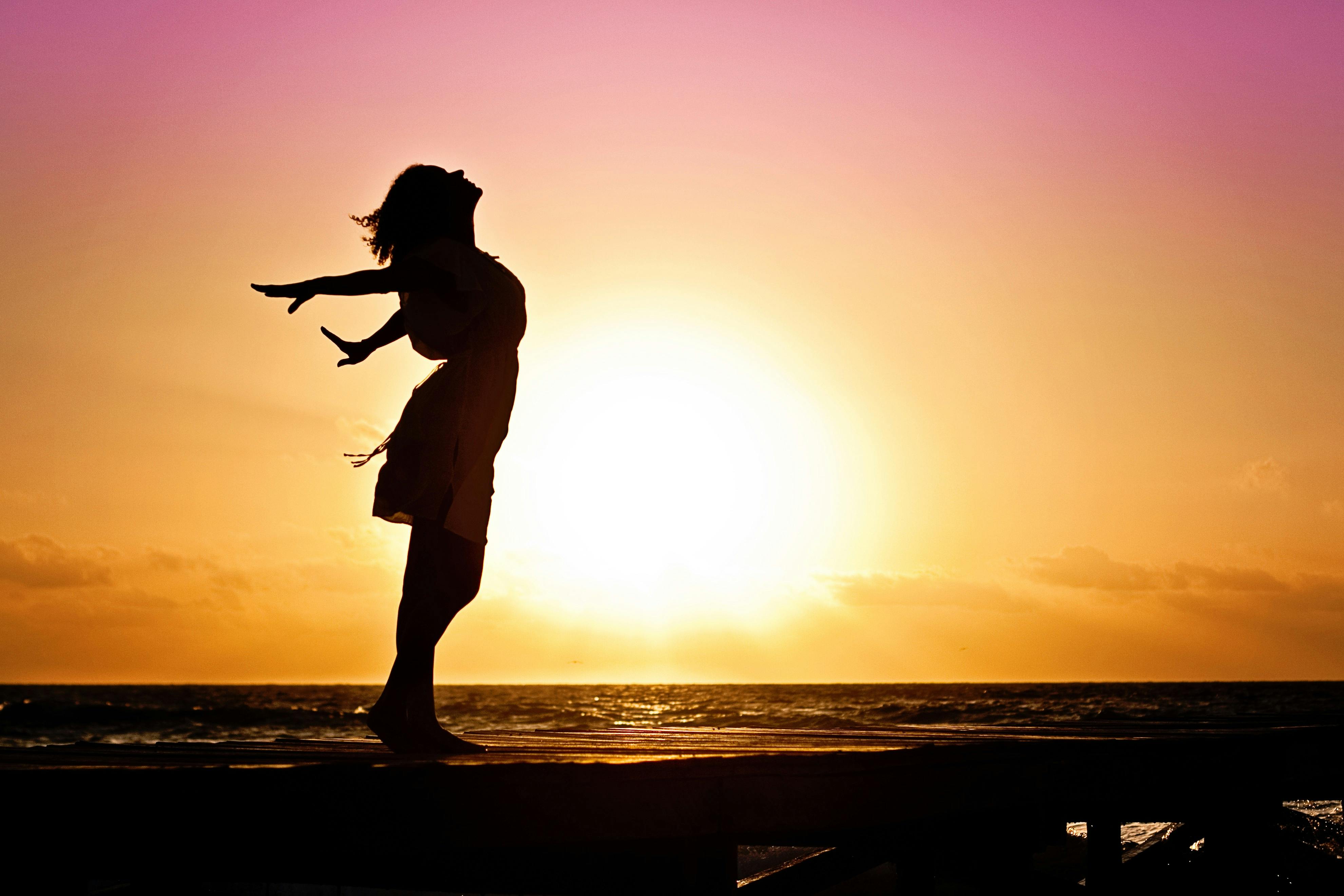 Silhouette of woman at beach sunset — freedom and recovery
